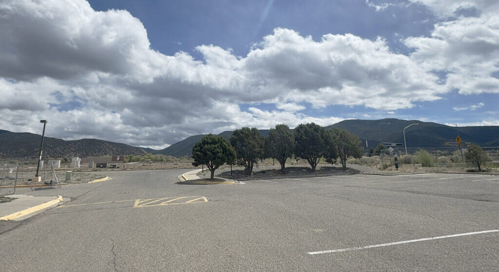 A parking lot with trees and mountains under a partly cloudy sky.