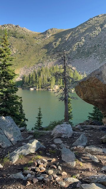 Scenic view of a mountain lake with pine trees and rocky terrain under a clear blue sky.