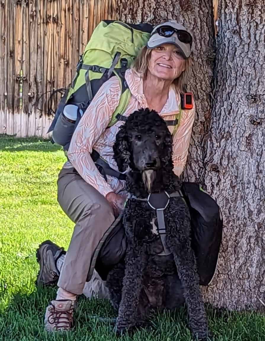 Hiker with a black dog resting by a tree during the Santa Fe to Taos Thru-Hike.