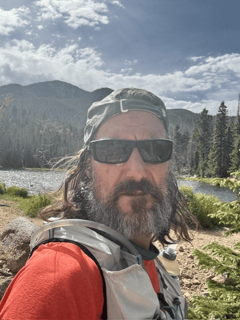 Hiker with sunglasses and backpack in scenic mountain landscape during Santa Fe to Taos Thru-Hike.