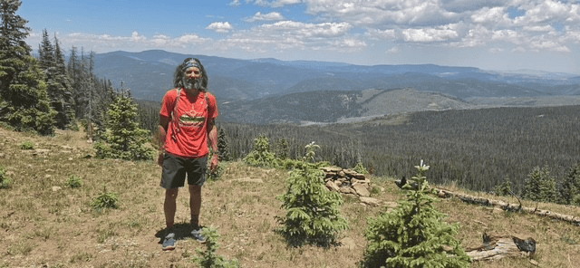 Hiker standing on mountain trail with scenic view of forests and mountains.